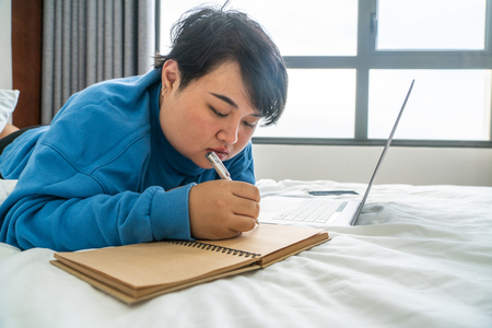 Asian woman lying on bed and writing diaryの写真素材