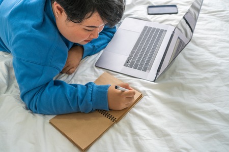 Asian woman lying on bed and writing diaryの写真素材