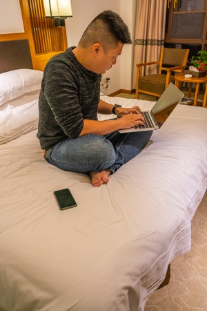 Young man sitting on bed and using laptopの写真素材