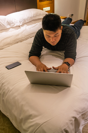 Young man lying on bed and using laptopの写真素材