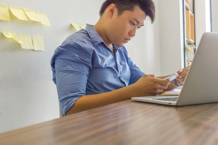 Young Asian man using phone in officeの写真素材