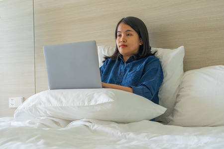 Young woman put laptop on pillow and workingの写真素材