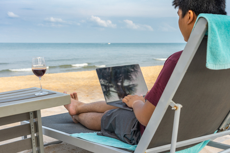 Freelancer working with laptop , red wine on beautiful summer beachの写真素材