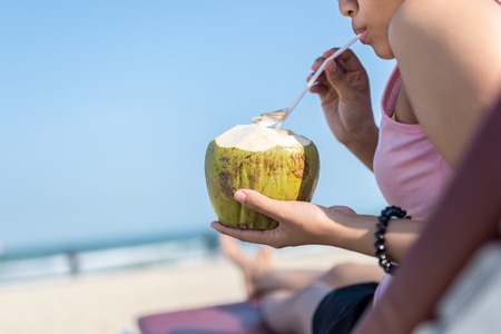 Close up of woman drinking fresh coconut juice at beachの写真素材