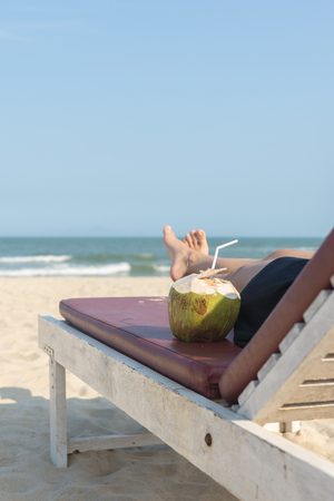 Close up of woman lying on beach chair with coconutの写真素材