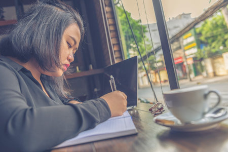 Freelance woman in black shirt writing next to laptop , coffee