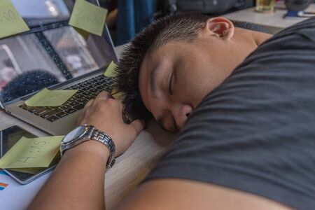 Exhausted office man fall asleep on desk with full of sticky notesの写真素材