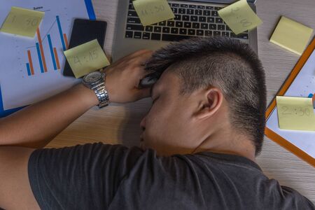 Tired freelancer sleeping on laptop next to paperworkの写真素材