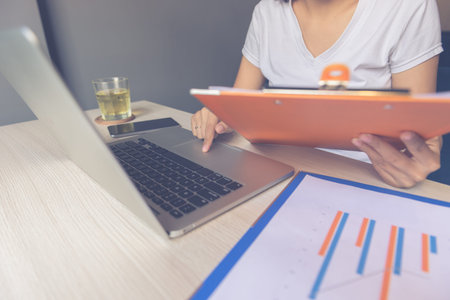 Woman using touchpad and holding document while working on laptop