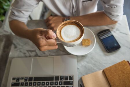 Close up photo of human hand holding cup of cappuccinoの写真素材