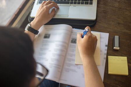 Rear view of student writing sticky note on workbookの写真素材