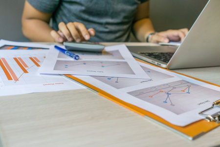 Human hands using calculator next to laptop and graph document