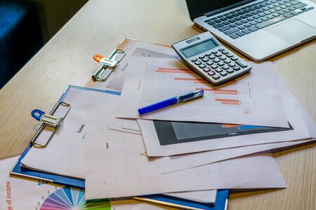 Busy cluttered working desk with laptop calculator and documentsの写真素材