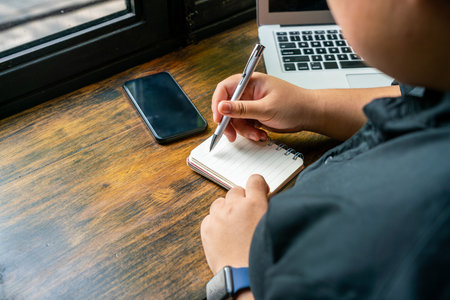 Freelancer writing daily notebook next to computer and cellphone