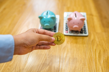 Businesswoman hand holding golden bitcoin with piggybank and calculators background