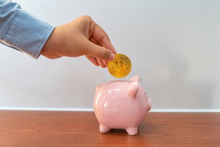 Businesswoman hand holding bitcoin and put it into piggy bankの写真素材