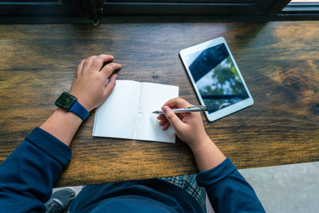 High angle view of human hand writing notebook next to tablet