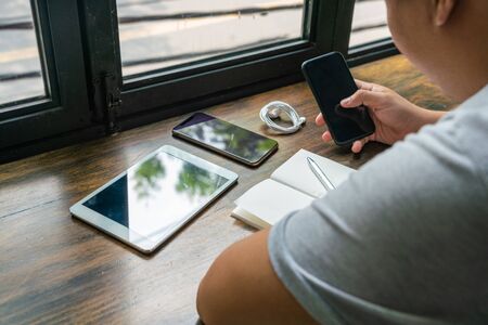 Asian freelancer using cellphone and other devices at rustic cafeの写真素材