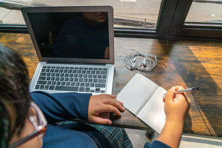 High angle view of woman writing notes next to laptop