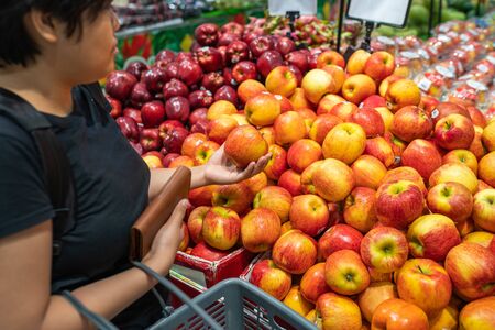 Asian woman picking apple at fruit stand in grocery storeの写真素材