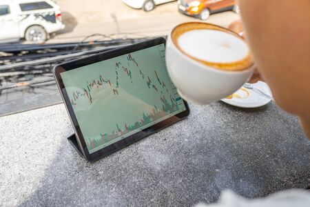 Businessman having coffee and watching stock trading graph on tabletの写真素材