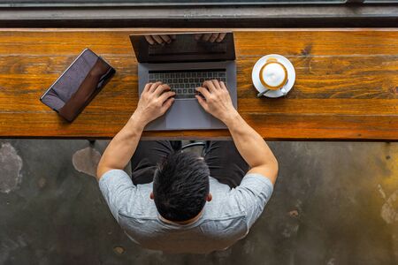 Asian freelancer typing laptop keyboard next to tablet at coffeeshopの写真素材