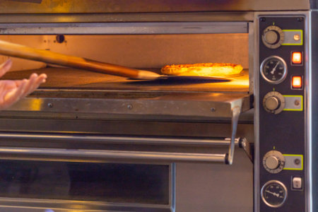 Baker using pizza shovel picking fresh baked pizza in oven