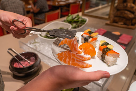 Human using tongs picking fresh sashimi and sushi in restaurantの写真素材