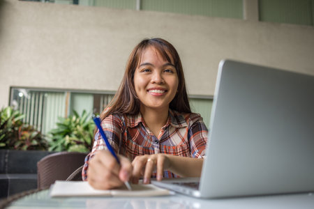 Smiling Asian lady working on laptop at outdoors cafeteria