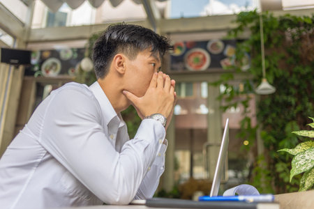 Frustrated Asian businessman sitting with laptop at coffee shop