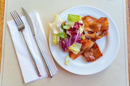 Grilled bacon ham slice and salad on white plate in restaurantの写真素材