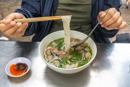 Human hand using chopsticks while having pho noodle soupの写真素材