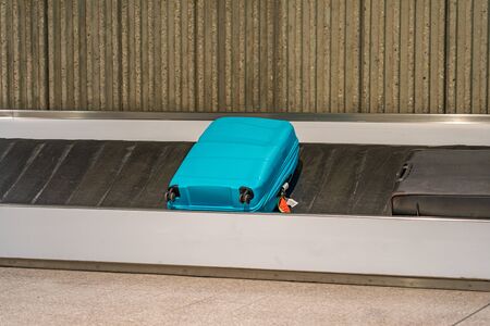 Blue suitcase laying on luggage conveyor belt at airportの写真素材