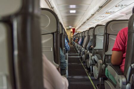Walking aisle in economy class cabin with passengers on the seatsの写真素材