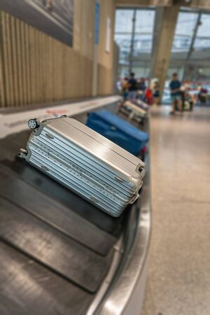 Vertical photo of silver colored suitcase on luggage conveyor beltの写真素材