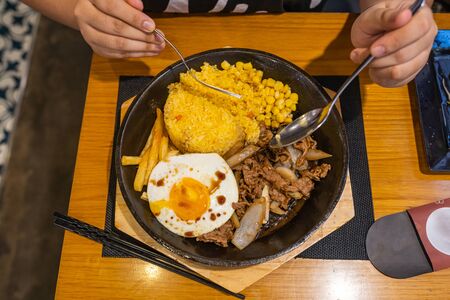 People eating sizzling beef sisig rice and fries on iron platterの写真素材