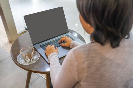 Modern woman using laptop while sitting at coffee tableの写真素材