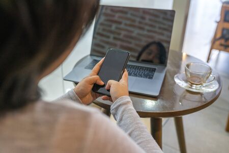 Asian woman using smartphone and laptop at coffee tableの写真素材
