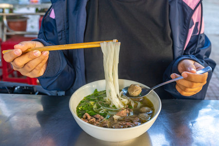 Female tourist having popular Vietnamese Pho bowl at street food vendor