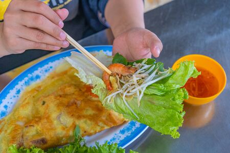 Human eating Banh Xeo crepe with lettuce and fish sauceの写真素材