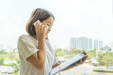 Asian businesswoman holding document and hearing phone callの写真素材