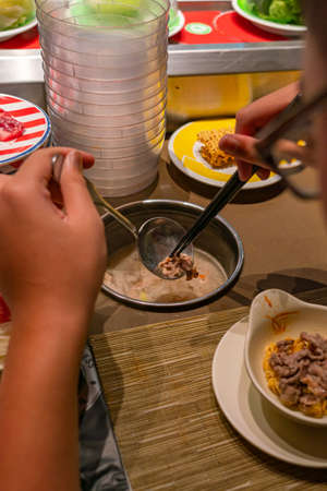 Close up photo of woman eating at conveyor belt hotpot restaurantの写真素材
