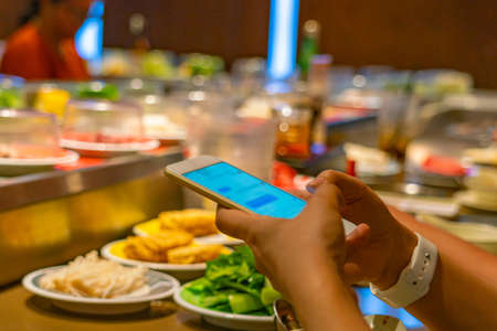 Close up photo of people using smartphone while eating at restaurantの写真素材