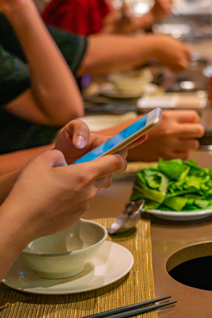 Close up photo of human using smartphone while eating with friendsの写真素材