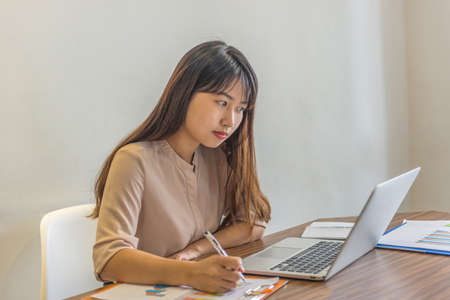 Young freelancer writing notes and working on laptop at homeの写真素材