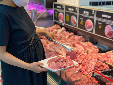 Pregnant woman wearing mask and buying pork meatの写真素材