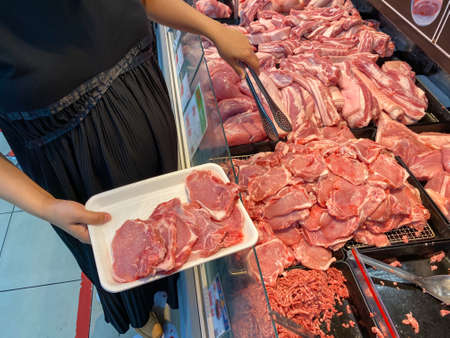 Pregnant woman buying raw pork chops at butcher shopの写真素材