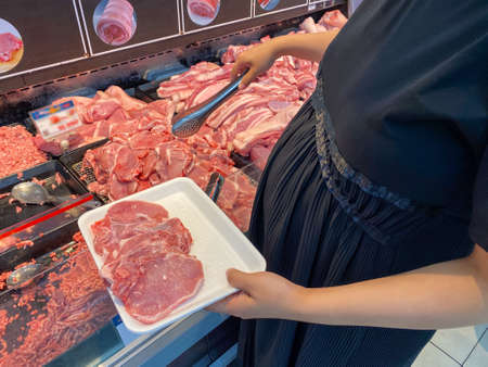 Pregnant woman with big belly buying pork meat in supermarketの写真素材