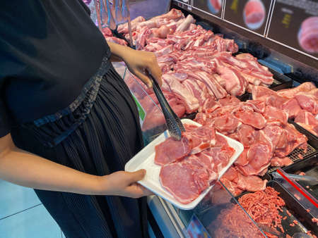 Pregnant woman choosing pork meat in supermarketの写真素材