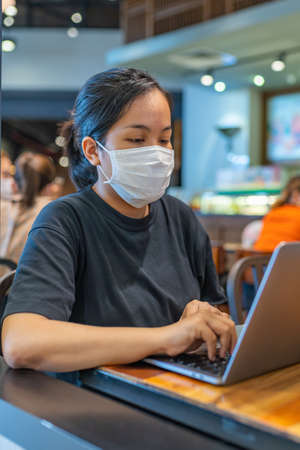 Vertical portrait of woman wearing protective mask and using laptopの写真素材